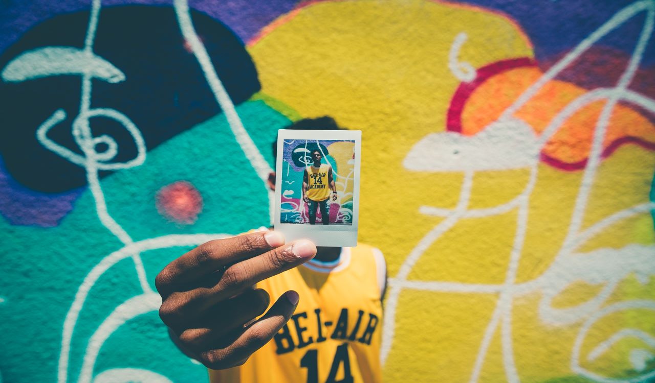 Man holding a photo of himself with a graffiti background